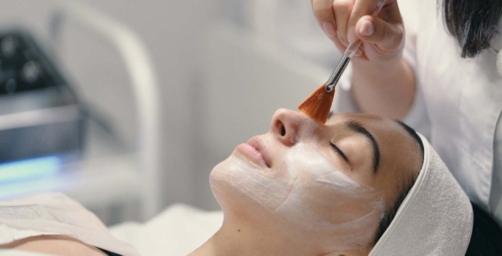 Beauty therapist applying facial mask to woman in spa salon